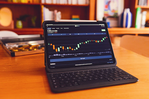 A tablet with a keyboard showing a stock candlestick chart resting on a table in a home library